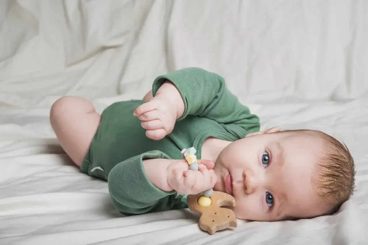 Kleines Baby mit blauen Augen spielt mit einem Holzbeißring. Vielleicht ist das der erste Zahn, der bald kommt.