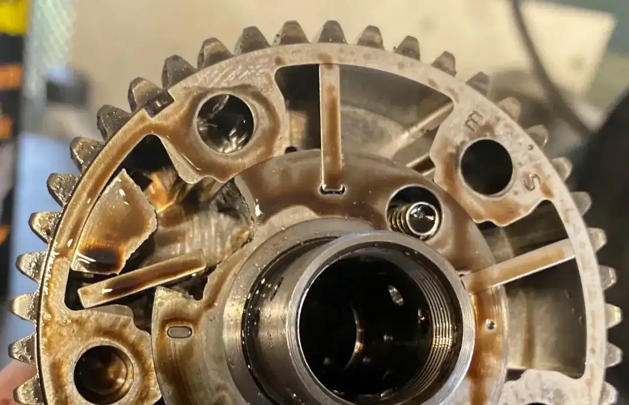 Uszkodzony element mechanizmu zmienne fazy rozrządu, z widocznymi fragmentami metalu i olejem.