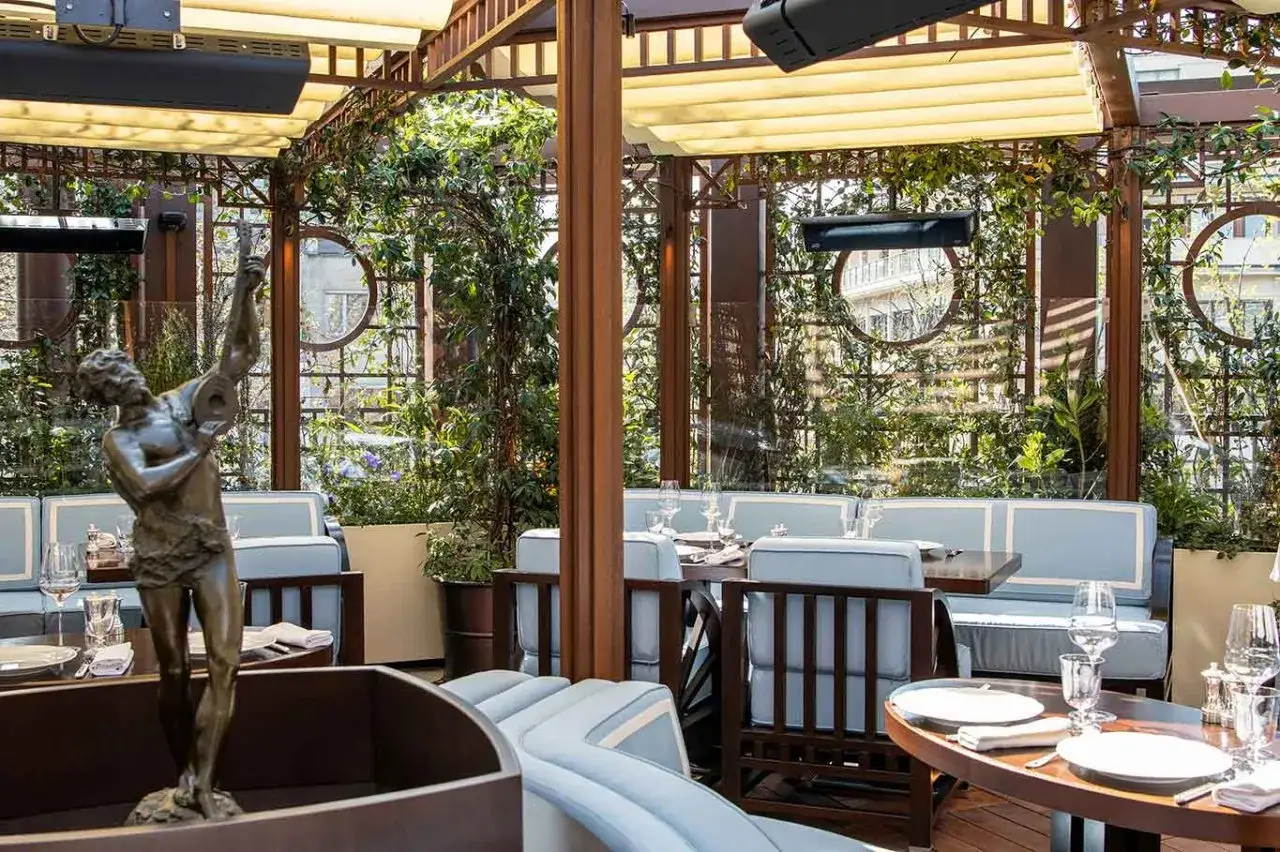 Terrazza elegante con divanetti azzurri e una statua, un'oasi verde che ricorda il fascino di the wilde milano.