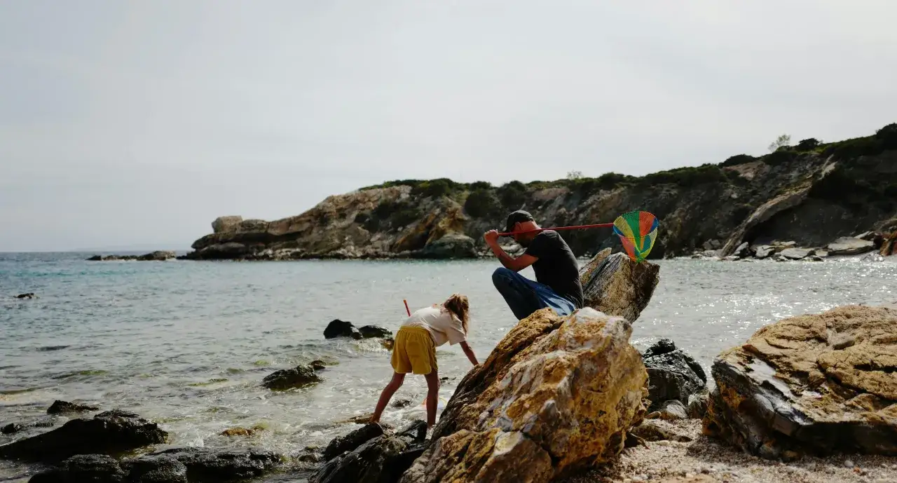 Padre e hija exploran la costa rocosa, buscando tesoros. Un plan perfecto de donde ir en Semana Santa con niños.