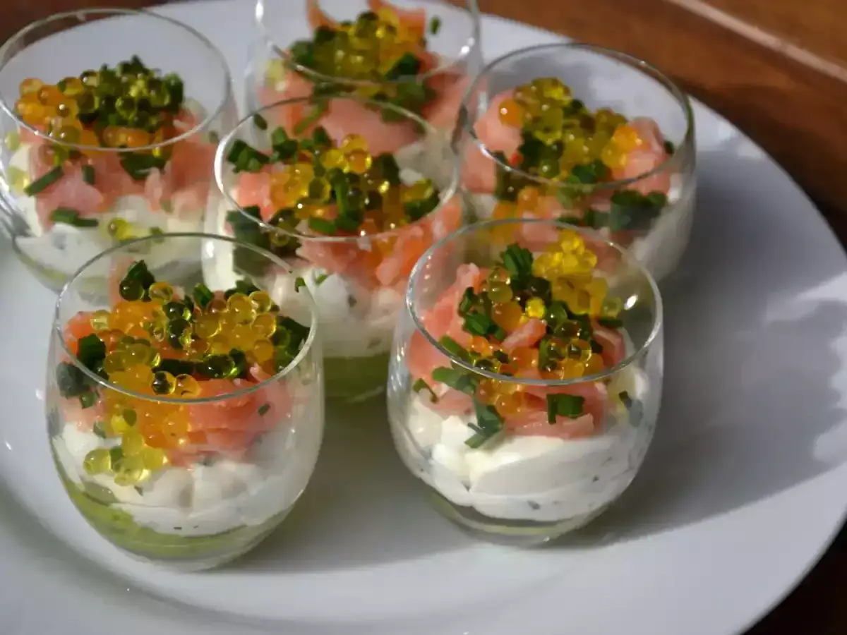 Six verrines avocat saumon, garnies de crème, saumon fumé, ciboule et perles d'orange et de jaune.