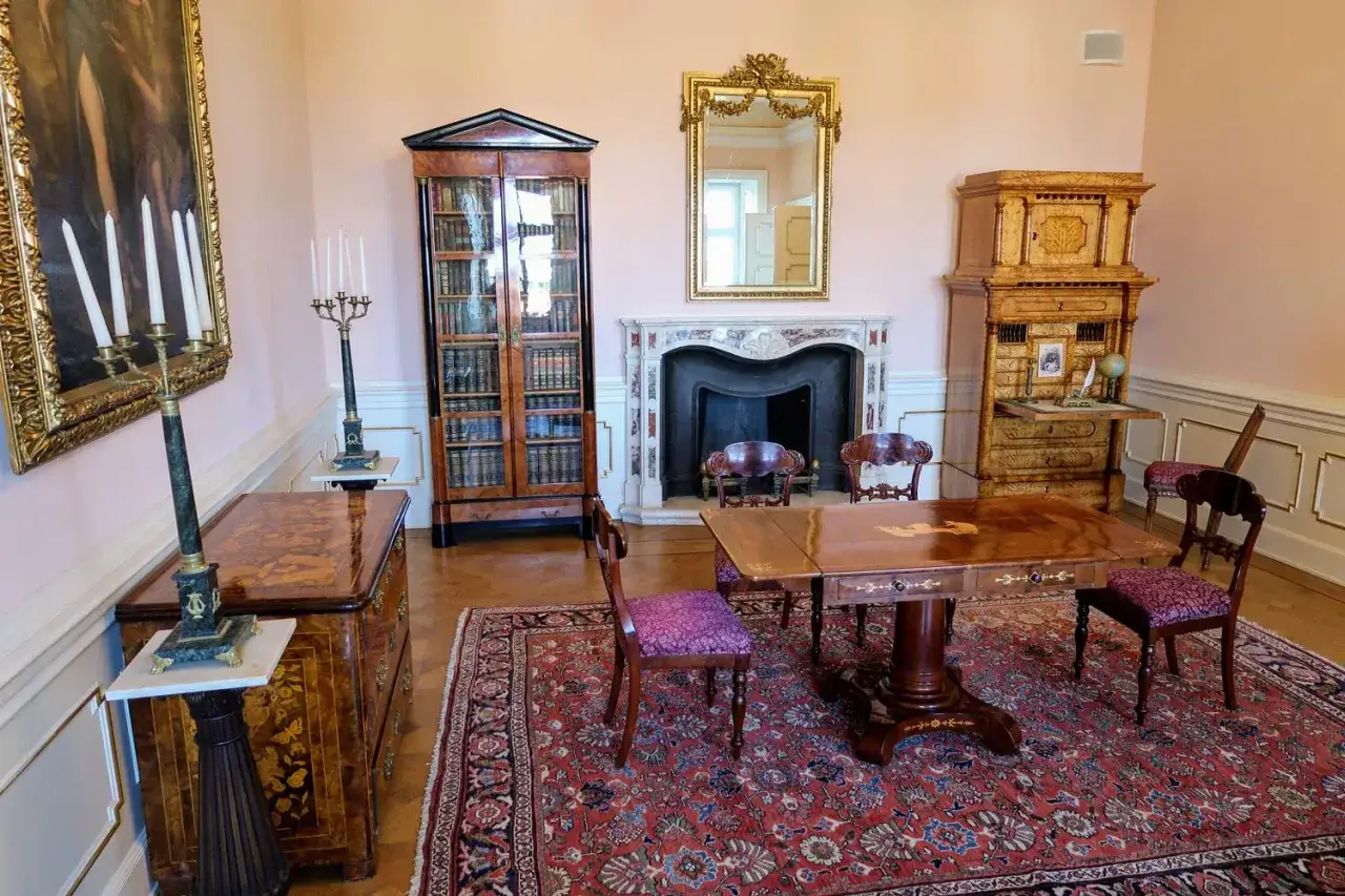 Elegancki salon w zamku książ. Biblioteka, kominek, biurko i stół z krzesłami tworzą atmosferę dawnych czasów.