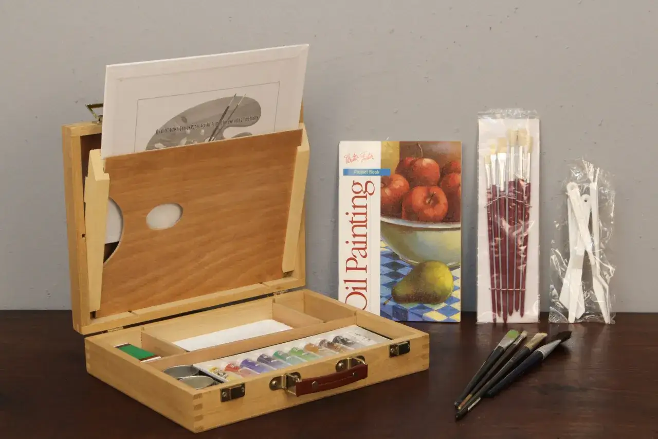 Une boîte en bois ouverte révèle des tubes de peinture à l'huile, des pinceaux et un livre de projets. La peinture à l'huile, c'est bien difficile, mais ce kit semble prêt à relever le défi.