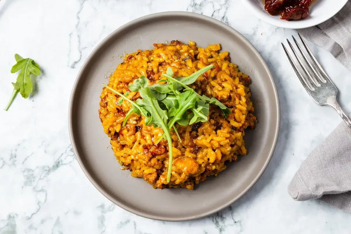Cremiges Risotto mit Salsiccia, garniert mit Rucola, auf einem grauen Teller.