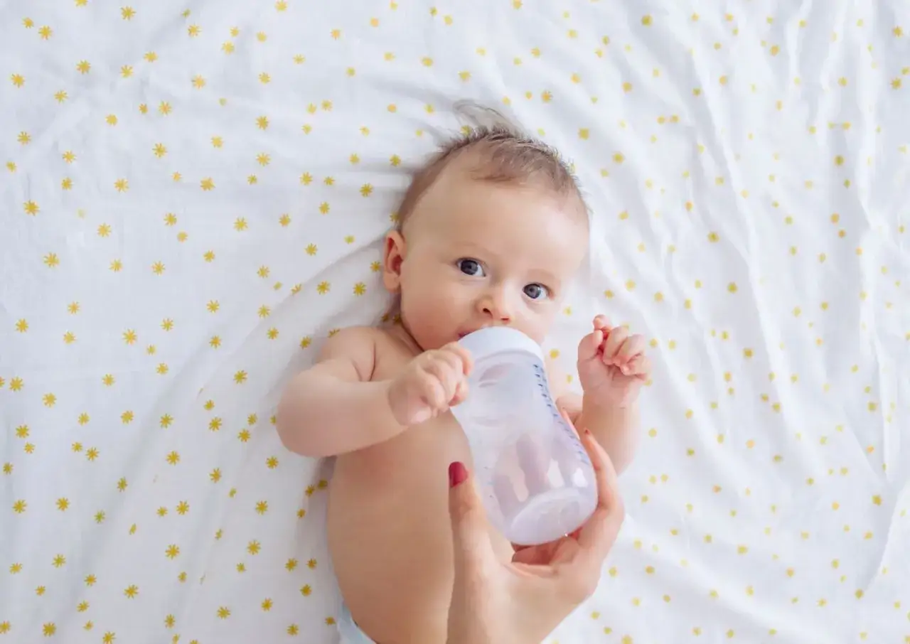 Niemowlę pije z butelki. Mama karmi dziecko, które ma lekką jelitówkę.