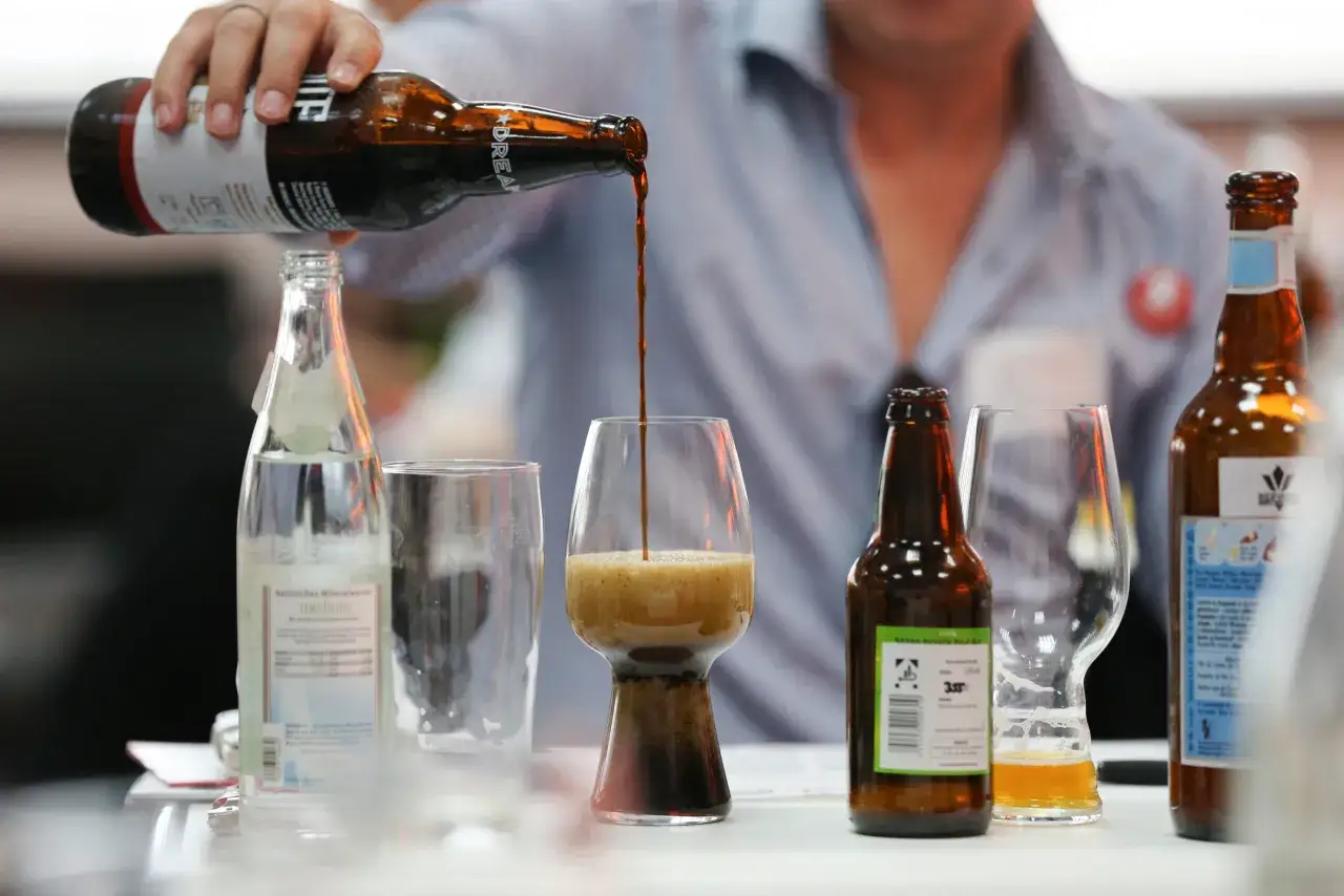Ein Mann gießt ein **IPA India Pale Ale** aus einer Flasche in ein Glas. Daneben stehen weitere Bierflaschen und Gläser.