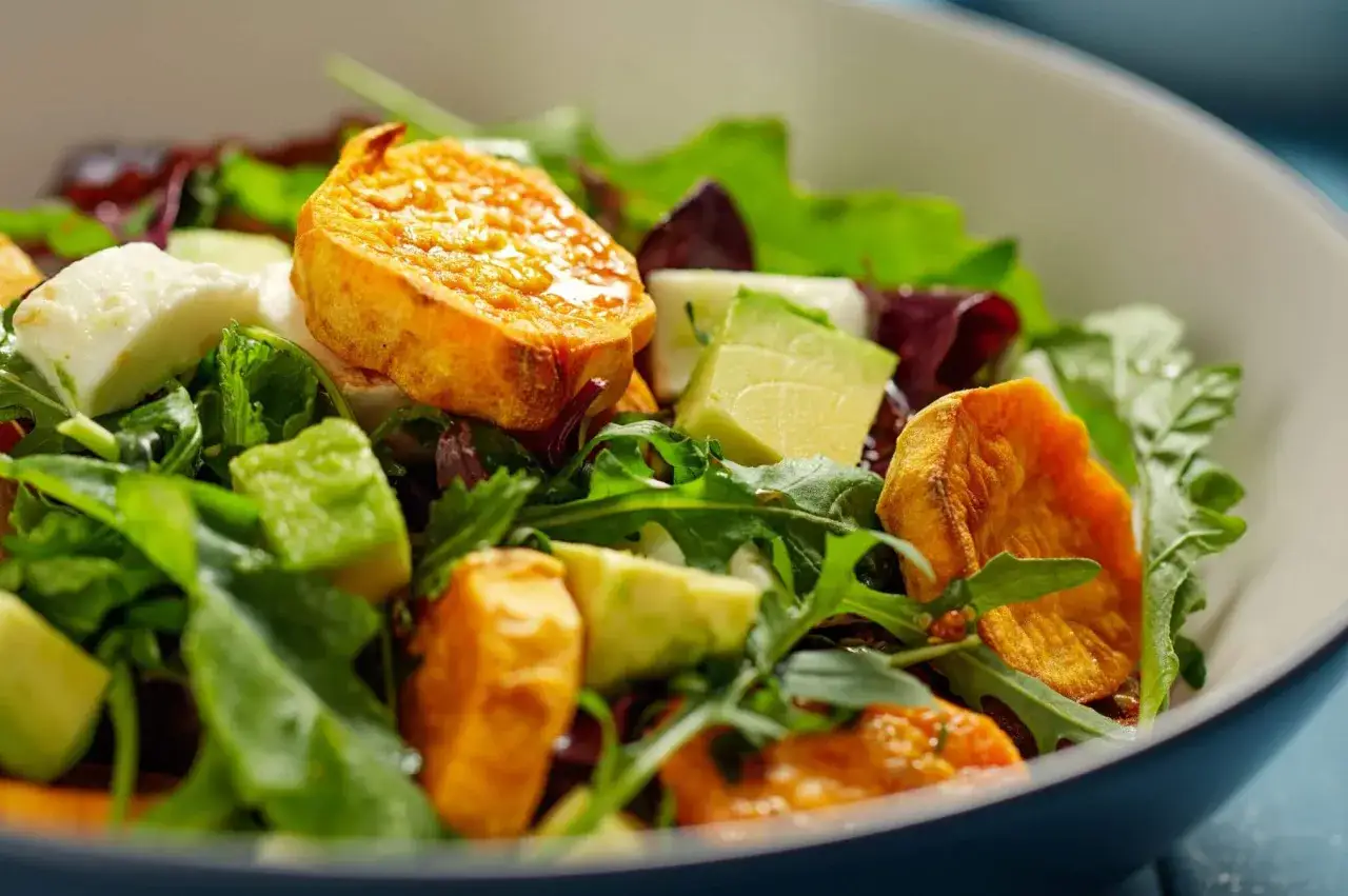 Ensalada fresca con trozos de aguacate, queso blanco y crujientes patatas fritas de boniato.