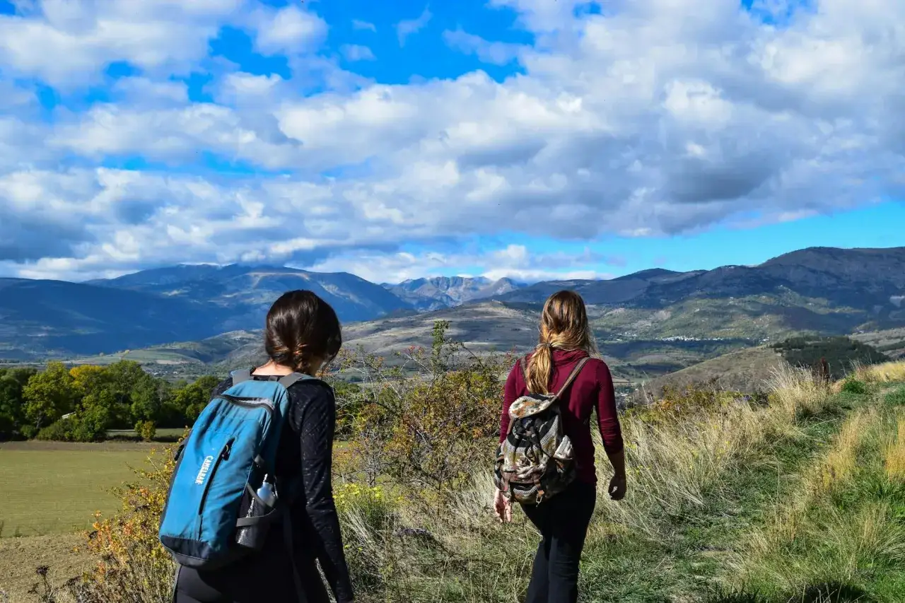 Dwie kobiety z plecakami podziwiają górski krajobraz. To jest właśnie co to jest hiking – wędrówka po górach.