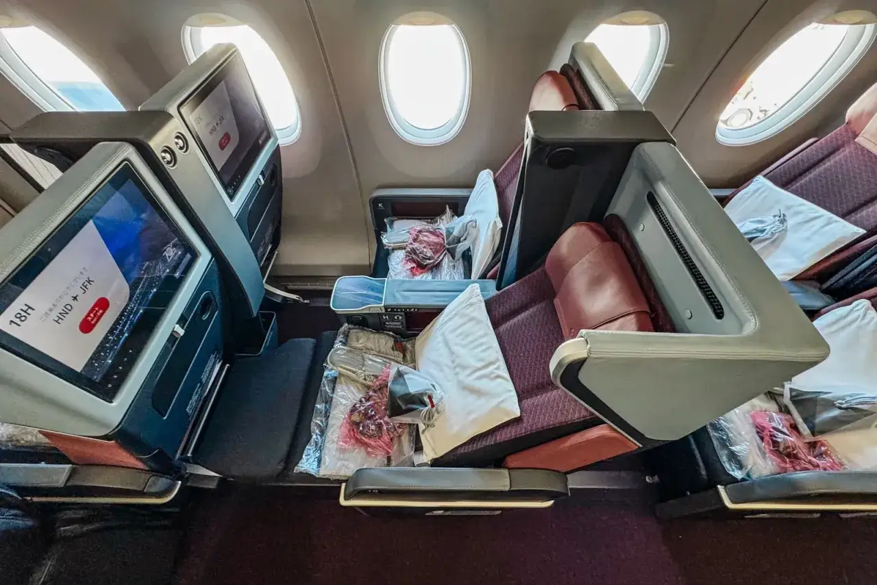 Luksusowe fotele w klasie biznes, gotowe na długi lot. Ekran pokładowy wyświetla trasę HND-JFK.