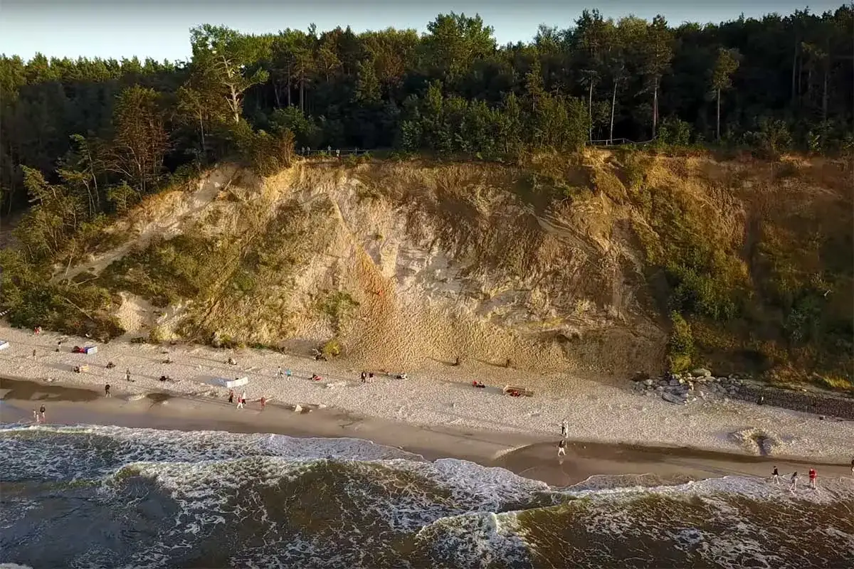 Jastrzębia Góra, gdzie klif niczym gwiazda północy wznosi się nad plażą. Ludzie spacerują po piasku, fale obmywają brzeg.