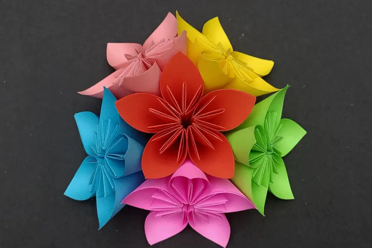 Bunte origami blumen, arrangiert in einem Kreis auf schwarzem Hintergrund.