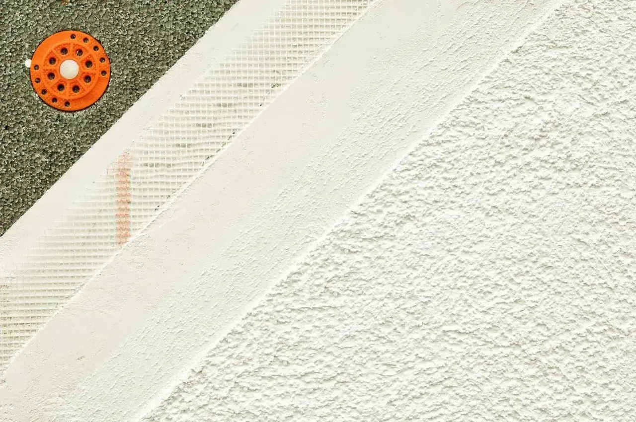 Warstwowa struktura elewacji z różnymi rodzajami tynków: styropian, siatka zbrojąca, gładź i tynk strukturalny.