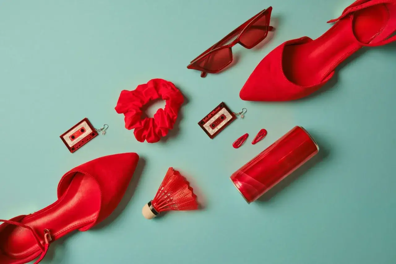 Flat lay d'accessoires rouges : escarpins, lunettes, chouchou, boucles d'oreilles cassette, barrettes, volant de badminton et canette.