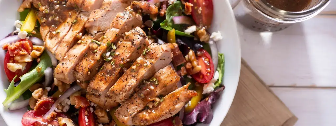 Deliziosa insalata estiva gourmet con pollo grigliato, pomodorini, cipolla rossa, noci e formaggio feta. Perfetta per un pasto leggero e saporito.
