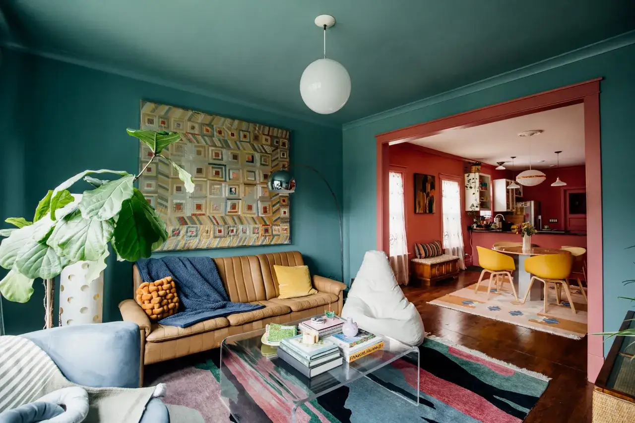 Salon z kanapą, rośliną i kolorowym dywanem. W tle widać jadalnię z ż&oacute;łtymi krzesłami. To prawdziwy **dopamine decor**!