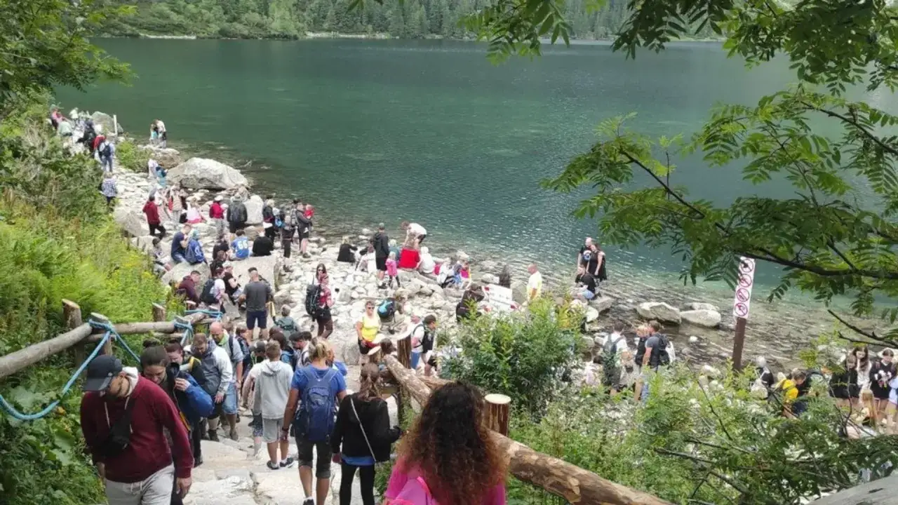 Tłum turystów wędruje kamienistym szlakiem nad brzegiem Morskiego Oka. Widać, ile się idzie nad Morskie Oko, by podziwiać piękno Tatr.