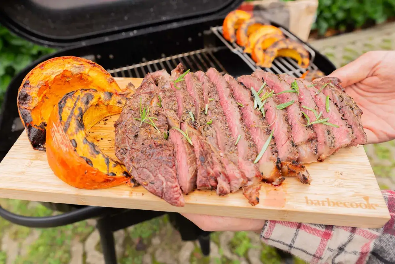 Un steak grillé et des quartiers de potimarron barbecue sur une planche en bois.