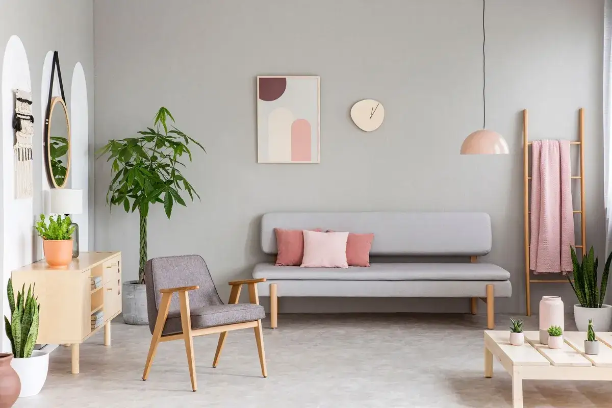 Un accogliente soggiorno con divano grigio, poltrona, tavolino e decorazioni in **rosa pastello**, come la coperta appesa alla scala di legno.