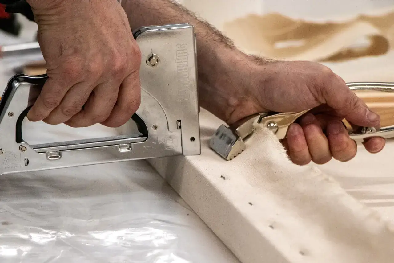 Comment tendre une toile sur un ch&acirc;ssis : mains utilisant une agrafeuse et une pince pour fixer la toile sur le bois.