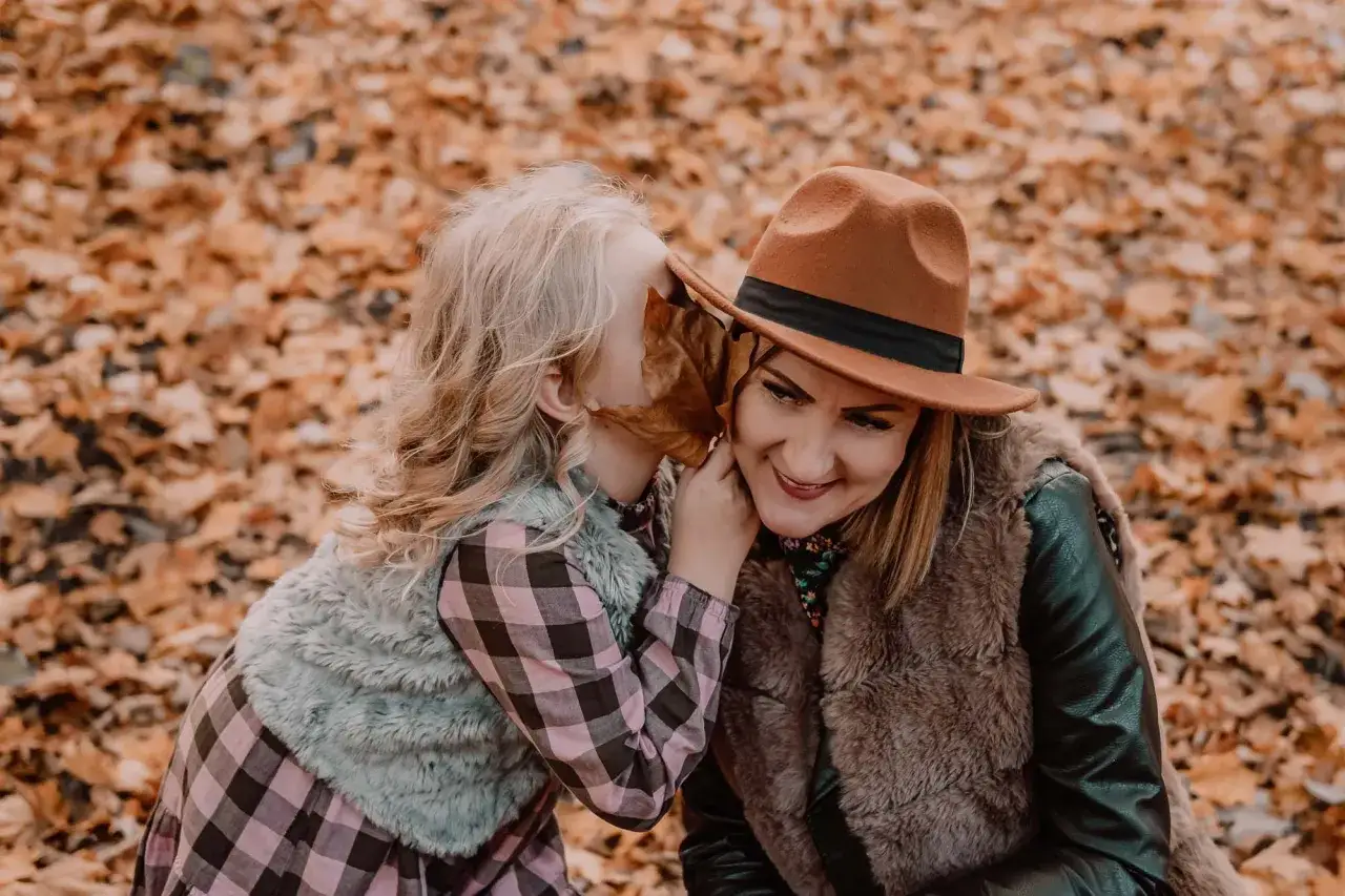 C&oacute;rka szepcze mamie sekret podczas sesji mama c&oacute;rka wśr&oacute;d jesiennych liści.