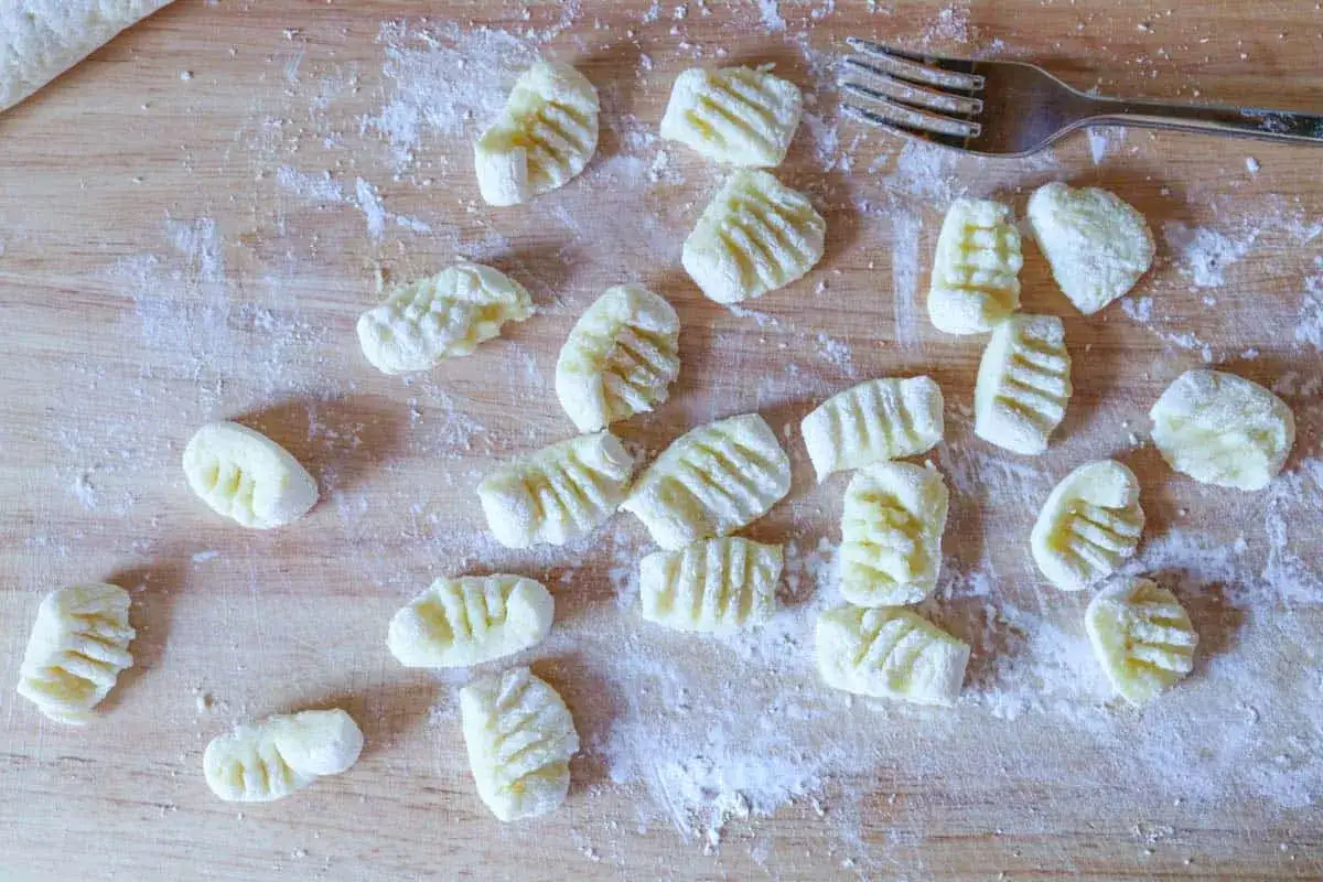 Frisch zubereitete Gnocchi liegen auf einem Holzbrett, best&auml;ubt mit Mehl. Eine Gabel liegt daneben, bereit, die n&auml;chste Portion Gnocchi zu formen.