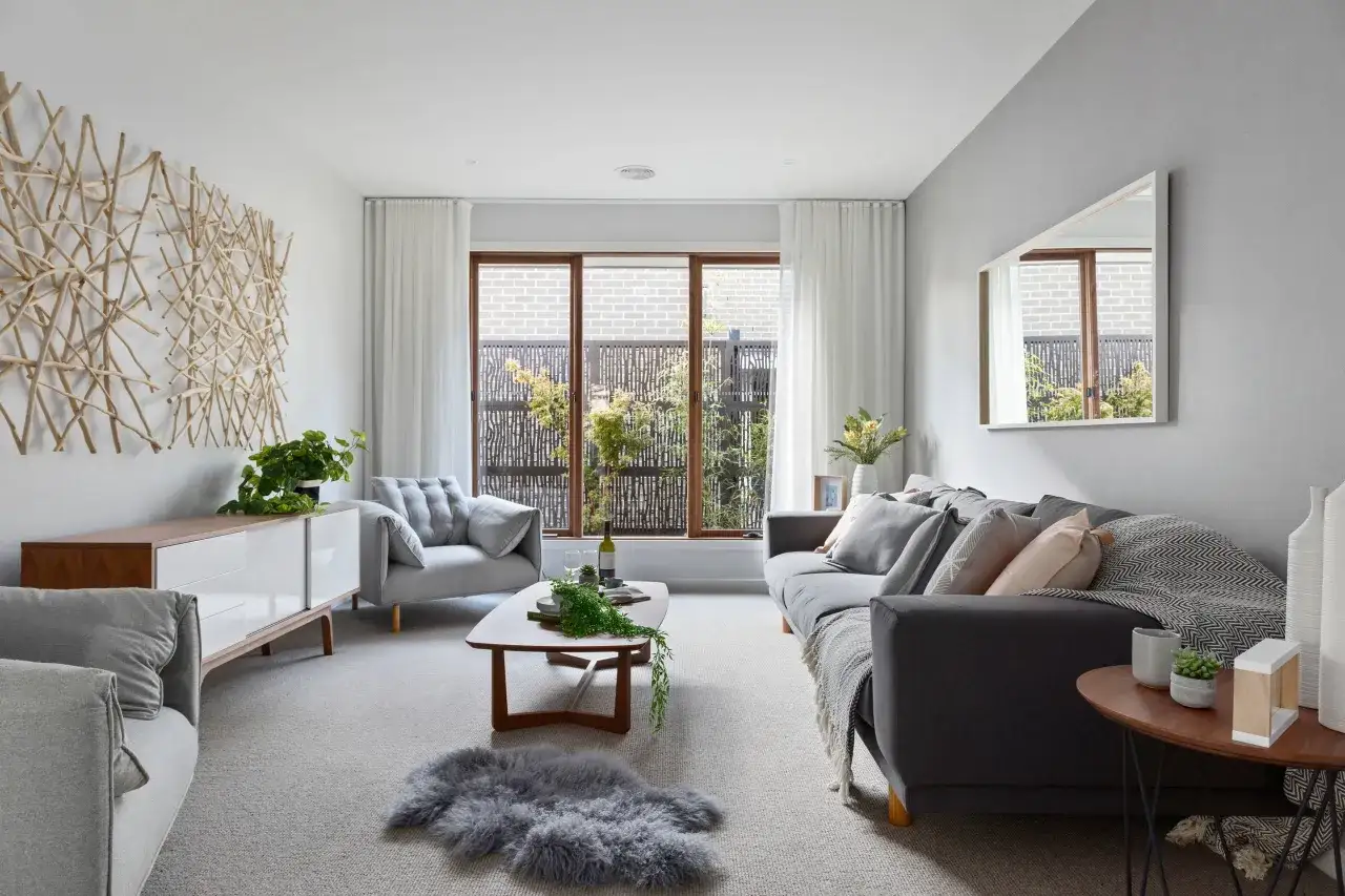Sof&aacute; gris y sill&oacute;n gris claro, con mesa de centro de madera. La decoraci&oacute;n de pared de ramas y la alfombra de piel gris crean un ambiente acogedor donde el beige y gris combinan a la perfecci&oacute;n.