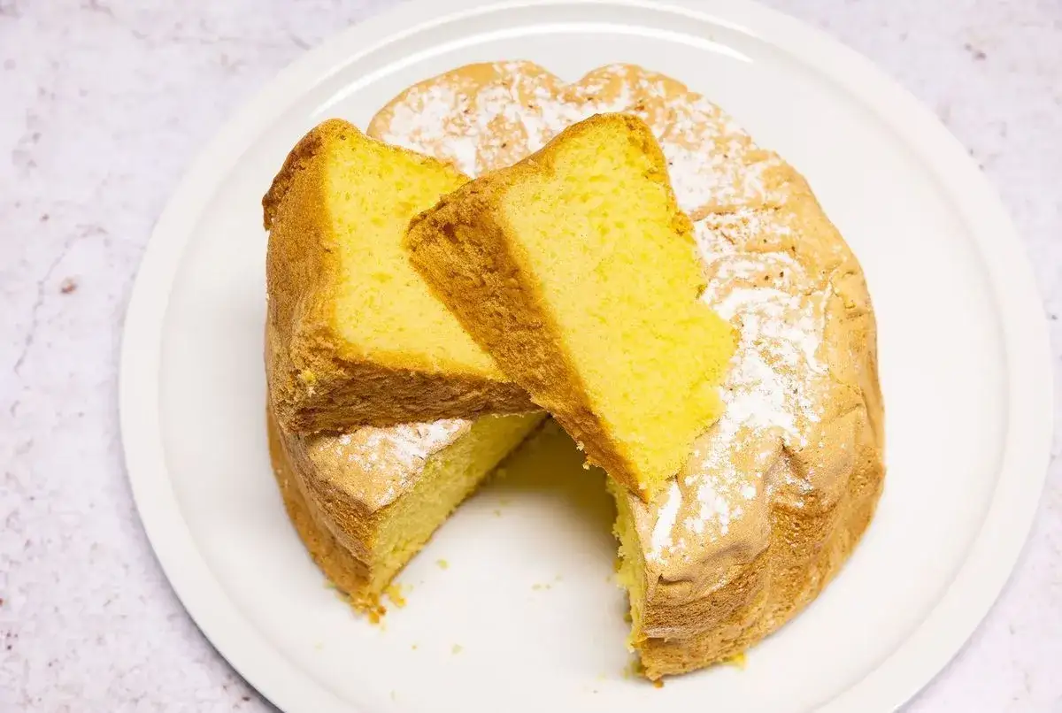 Un moelleux gâteau de Savoie, saupoudré de sucre glace, avec deux parts généreuses dressées sur le dessus.