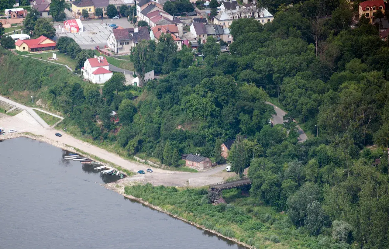 Wyszogr&oacute;d atrakcje: miasto nad Wisłą, z widokiem na zabudowania, zielone wzg&oacute;rza i rzekę z łodziami przy brzegu.