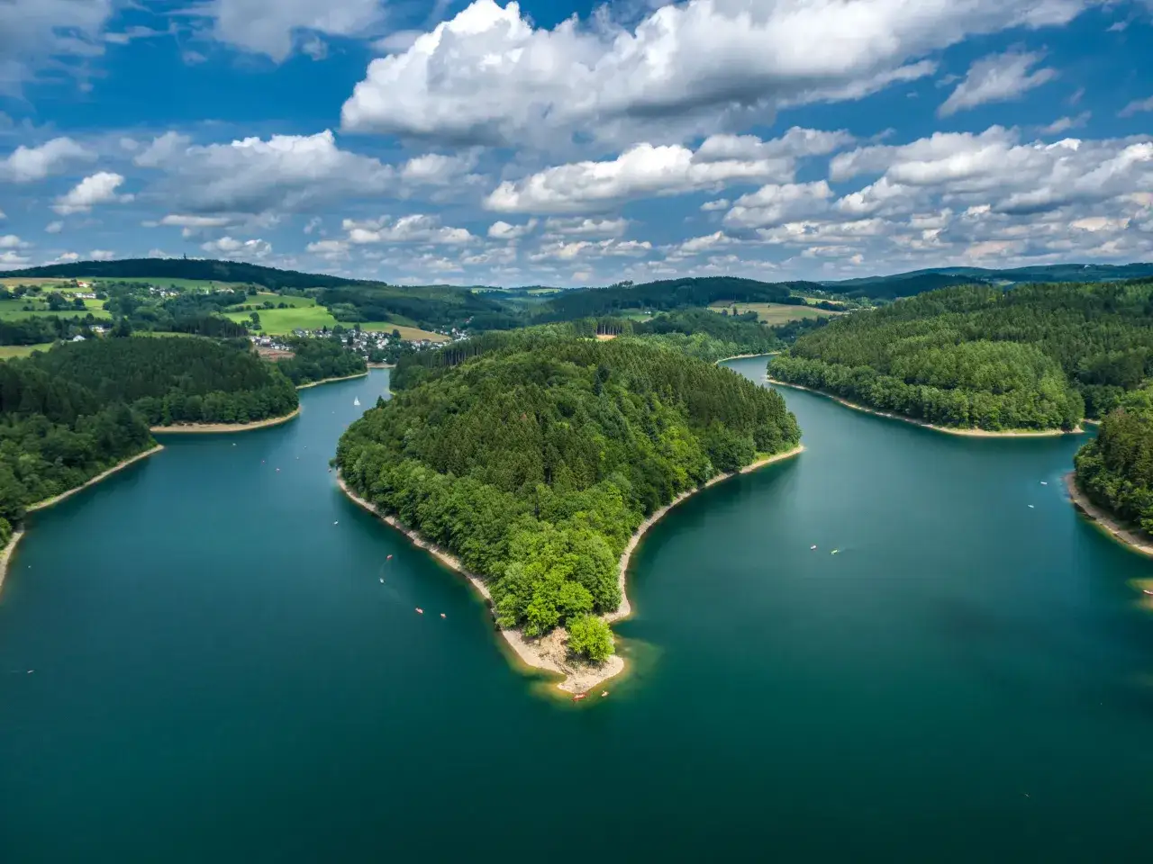 Grüne Hügel und ein türkisfarbener See mit kleinen Booten. Ein idyllisches Bild für Ausflugsziele NRW Wasser.