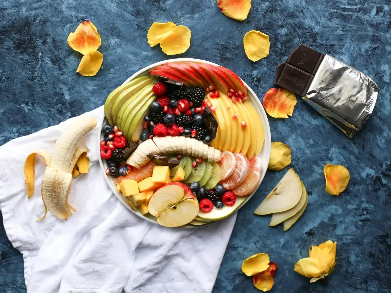 Kolorowa taca z owocami: jabłka, gruszki, mango, kiwi, cytrusy, jagody, maliny, jeżyny i kawałek gorzkiej czekolady. Czy to wszystko, co warto wiedzieć o fenyloalaninie?