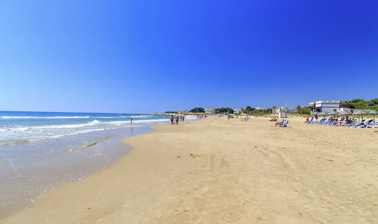 Playa de Alcossebre con gente paseando y tumbonas bajo sombrillas. Un día perfecto para saber qué hacer en Alcossebre.