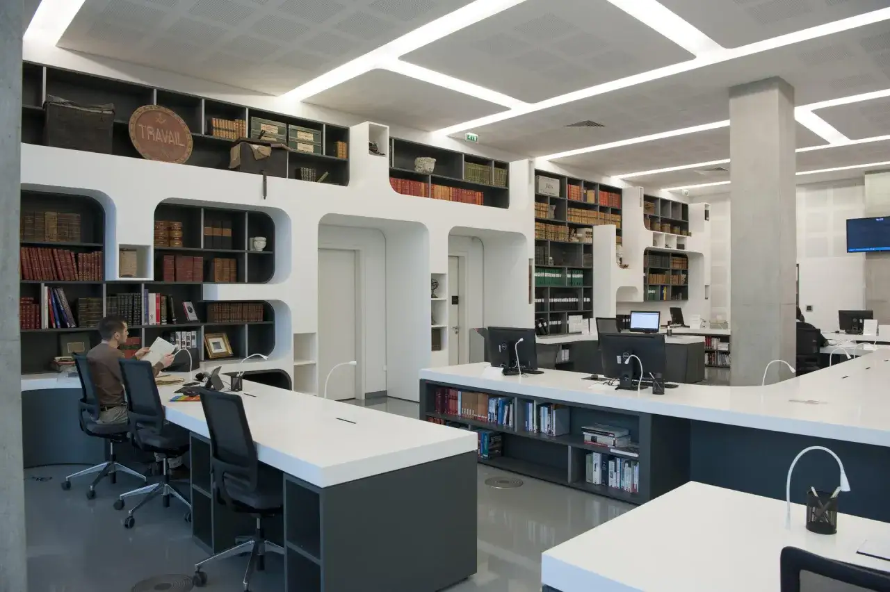 Salle de lecture moderne aux archives d&eacute;partementales 64, avec &eacute;tag&egrave;res remplies de livres anciens et postes de travail informatis&eacute;s.