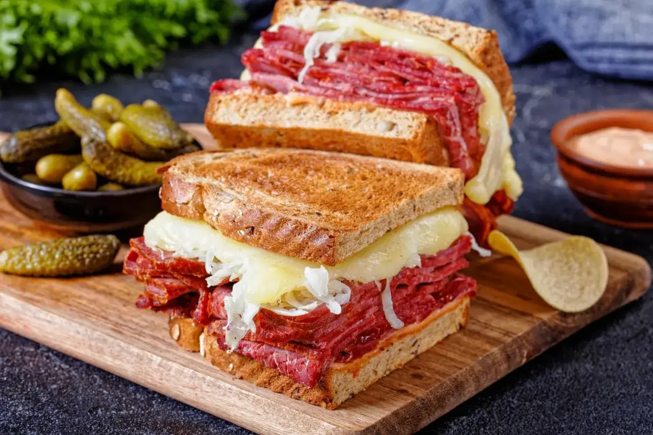 Pyszny reuben sandwich z dużą ilością wołowiny, sera i kiszonej kapusty, podany z ogórkami konserwowymi.