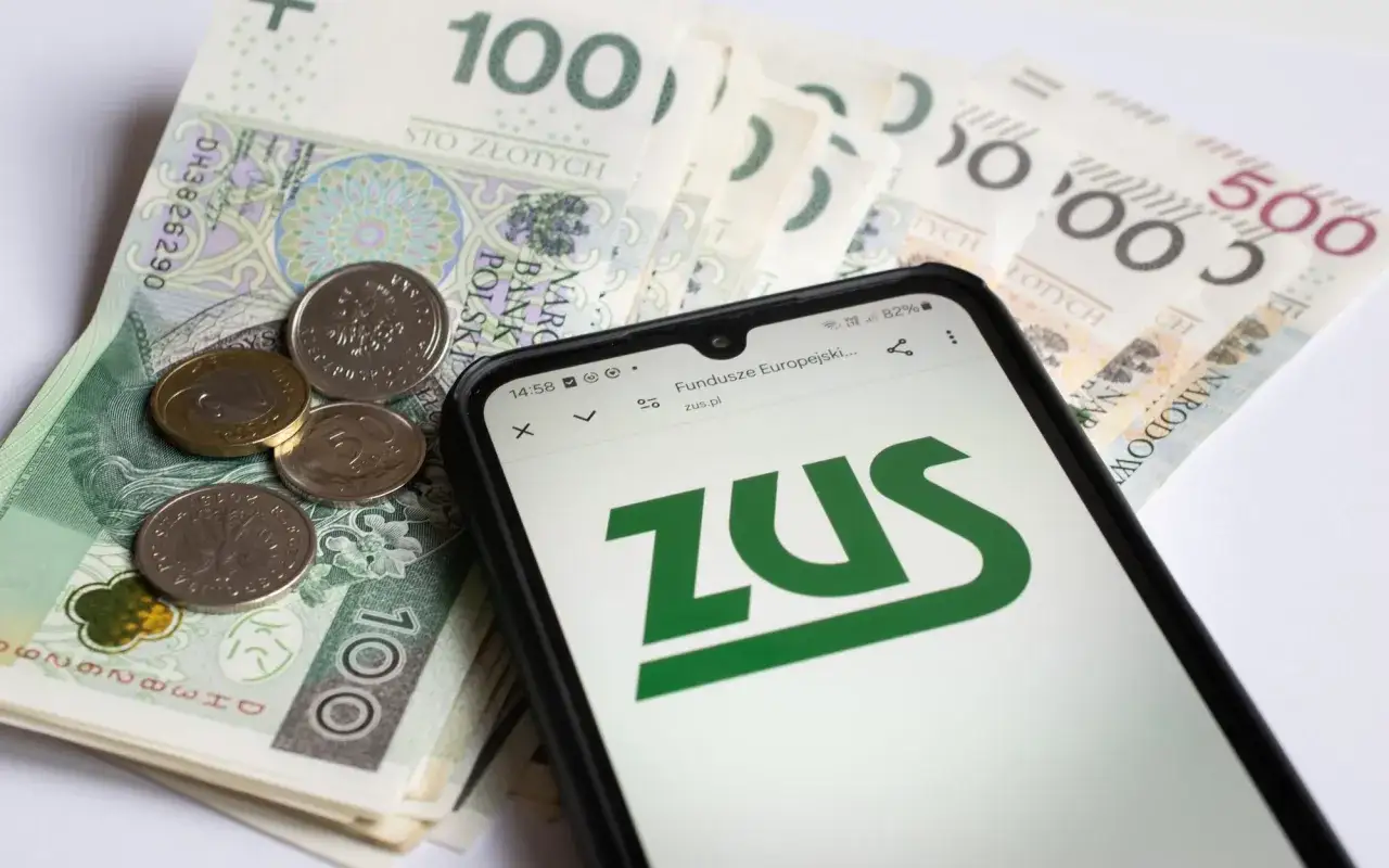 Złotówki i monety na stole, na nich smartfon z logo ZUS. To może być pomocne przy planowaniu, co to jest okresowa emerytura kapitałowa.