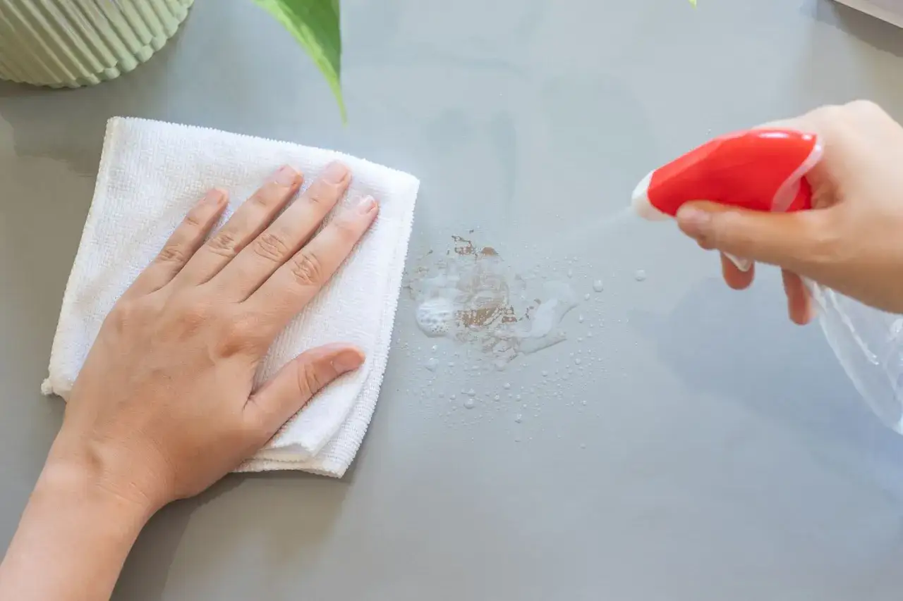 Handen torkar bort envisa tejprester med en vit trasa och sprayflaska.