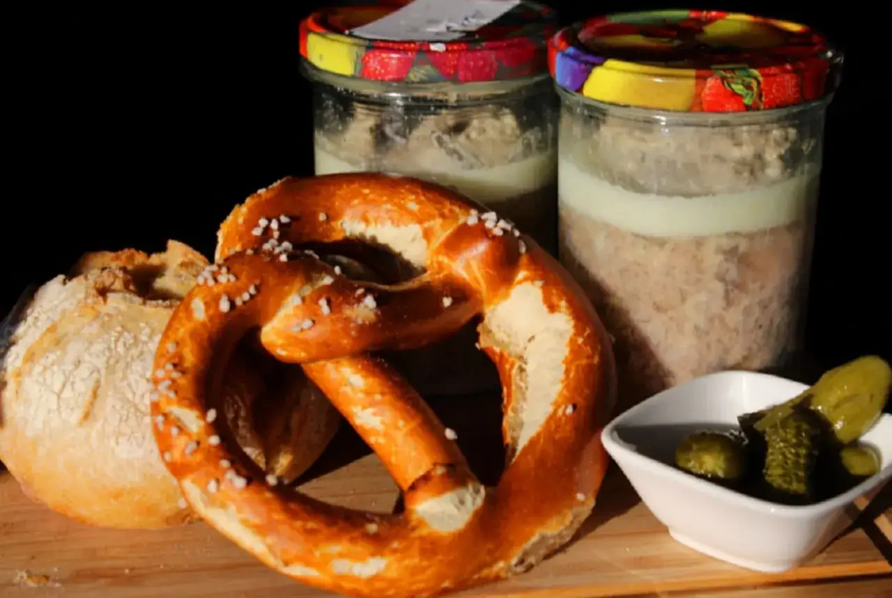 Gebratenes Fleisch einkochen: Zwei Gl&auml;ser mit Fleischkonserve, ein Brezel, Brot und Gew&uuml;rzgurken auf einem Holzbrett.