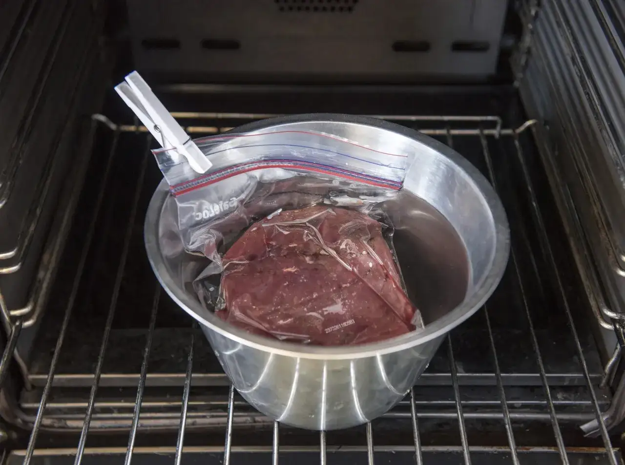 Vildsvinskött i vakuumpåse i en skål med vatten, redo för sous vide. Kontrollerar innertemp för perfekt resultat.