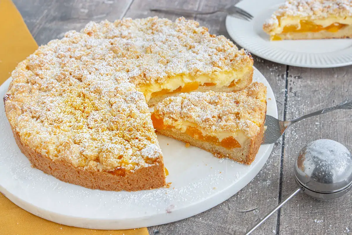 Ein saftiger aprikosenkuchen mit streusel, best&auml;ubt mit Puderzucker. Ein St&uuml;ck wird gerade serviert.