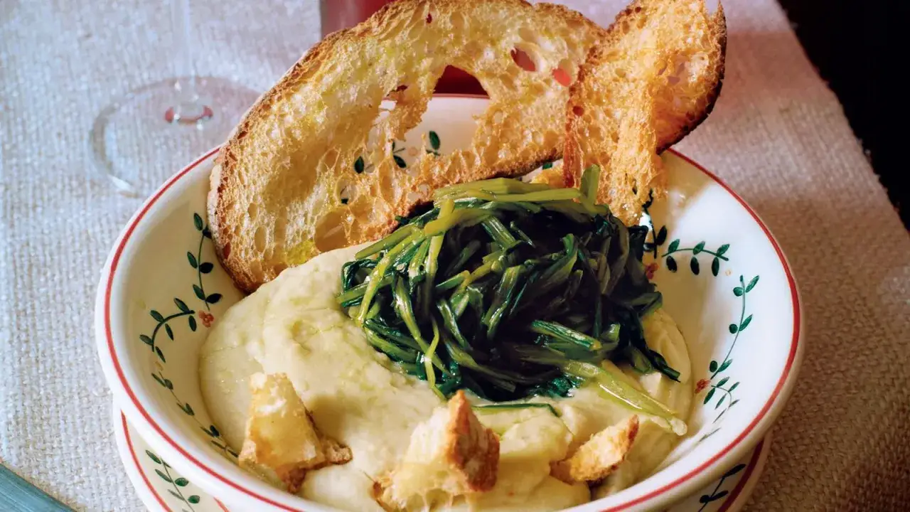 Piatto di fave e cicoria con crostini di pane abbrustolito, servito in una ciotola decorata.