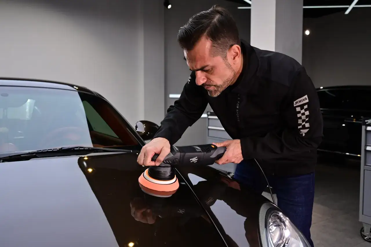 Man polerar en mörk bil med en polermaskin. Ett polerpaket kan ge bilen en spegelblank finish.