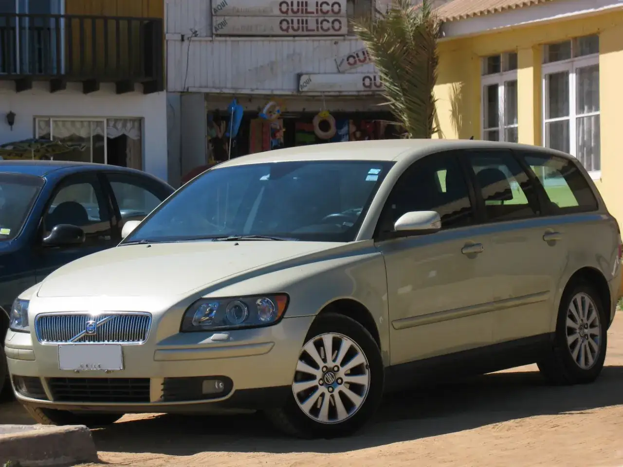 En ljusbeige Volvo V50 kombi st&aring;r parkerad framf&ouml;r en byggnad med skyltar. Denna modell &auml;r k&auml;nd f&ouml;r sina p&aring;litliga volvo v50 motorer.