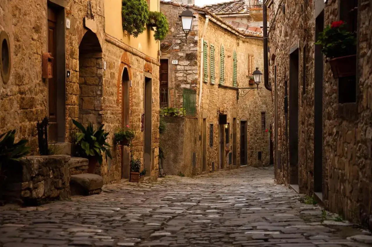 Un vicolo acciottolato tra antichi borghi vicino a San Casciano Val di Pesa. Case in pietra con finestre verdi e vasi di fiori creano un'atmosfera suggestiva.
