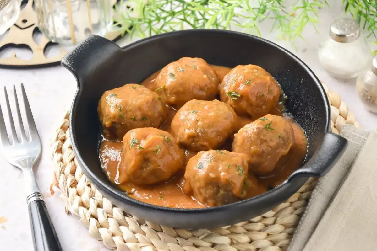 Sabrosas **albondigas en salsa** casera, servidas en una cazuela negra, listas para disfrutar con un tenedor.