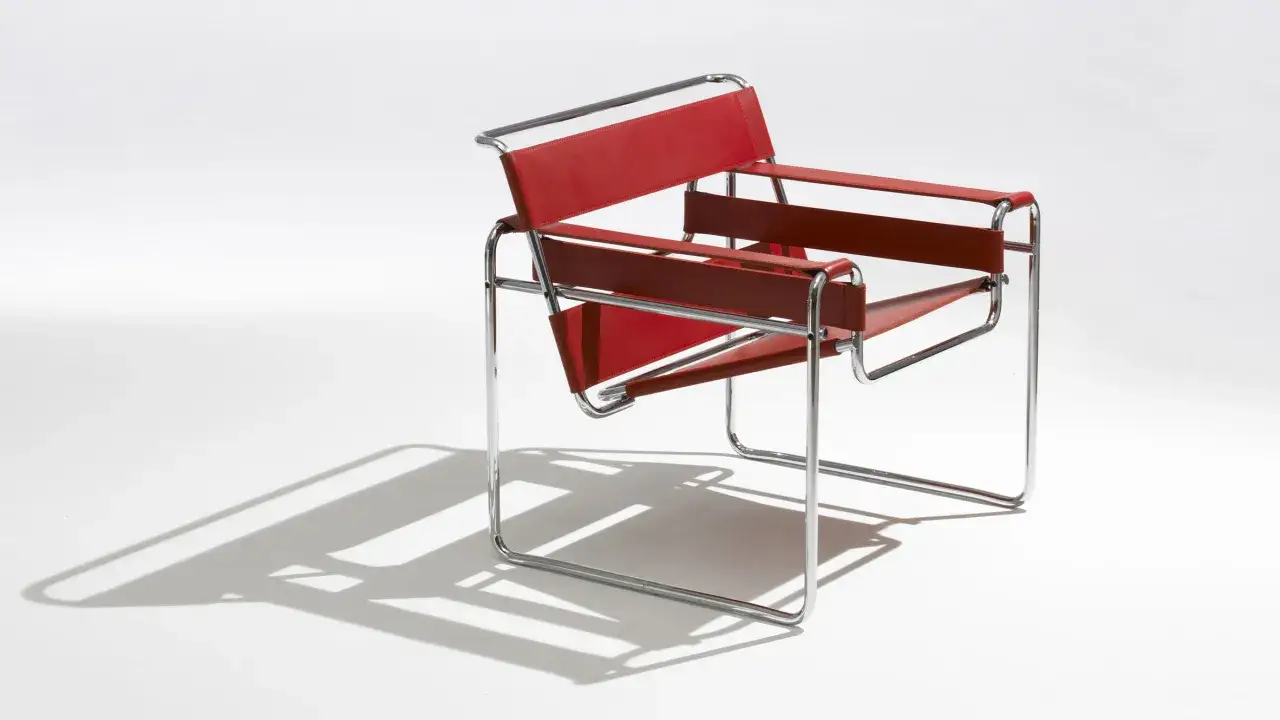 Iconica poltrona Wassily di Marcel Breuer, con struttura in tubolare cromato e seduta in cuoio rosso.