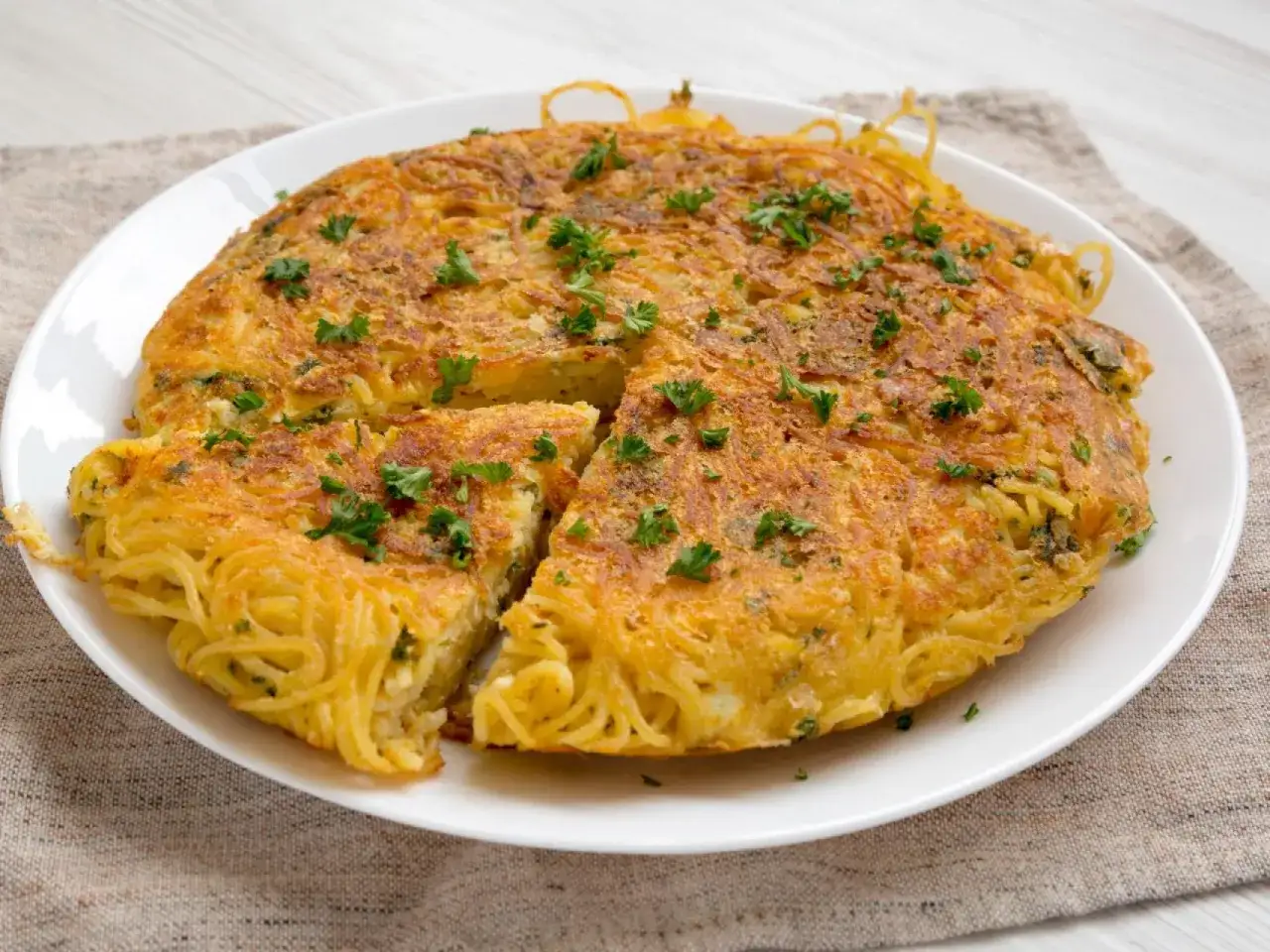 Tortilla de espaguetis dorada y esponjosa, adornada con perejil fresco. Un plato delicioso y original.