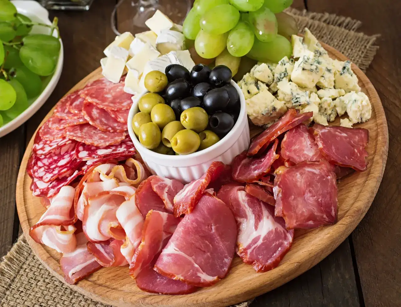Un invitante tagliere fai da te con salumi misti, formaggi, olive e uva verde, perfetto per un aperitivo.