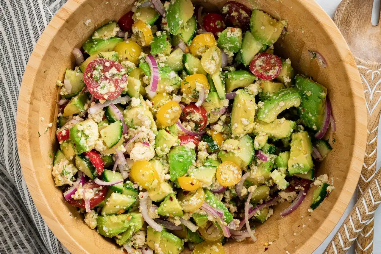 Frischer veganer Salat mit Avocado, Gurke, Tomaten und roten Zwiebeln in einer Holzschüssel.