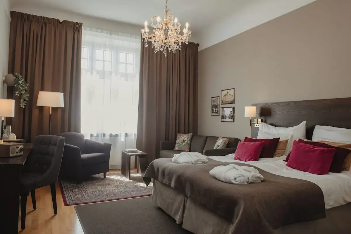 Ett elegant rum på hotel Drott Karlstad med stor säng, soffa, fåtölj och kristallkrona.