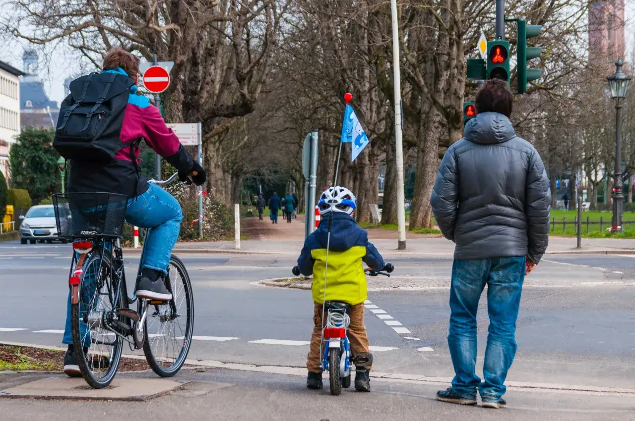 Ein Kind auf einem kleinen Fahrrad f&auml;hrt auf dem Gehweg in falsche Richtung, w&auml;hrend ein Erwachsener daneben steht.