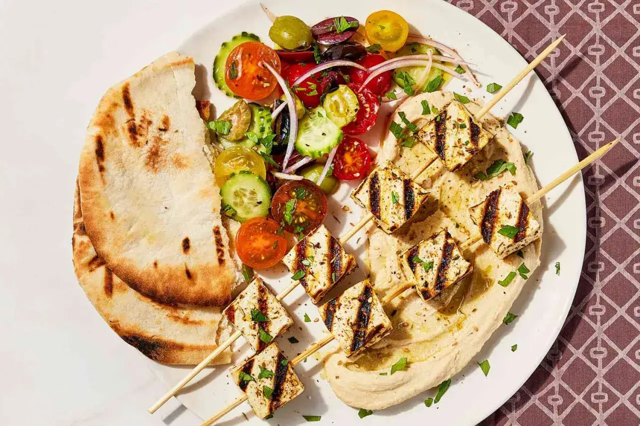 Grillowane szaszłyki z sera halloumi na kremowym hummusie, podane z pitą i sałatką z pomidorów, ogórka i oliwek. Idealne jedzenie na grilla.
